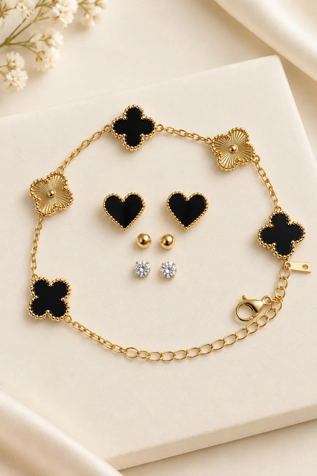 Black and gold clover bracelet laid flat with heart, ball and clear stone studs