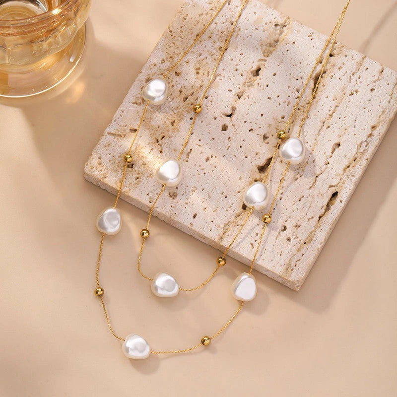 Layered pearl necklace on a stone block beside a glass