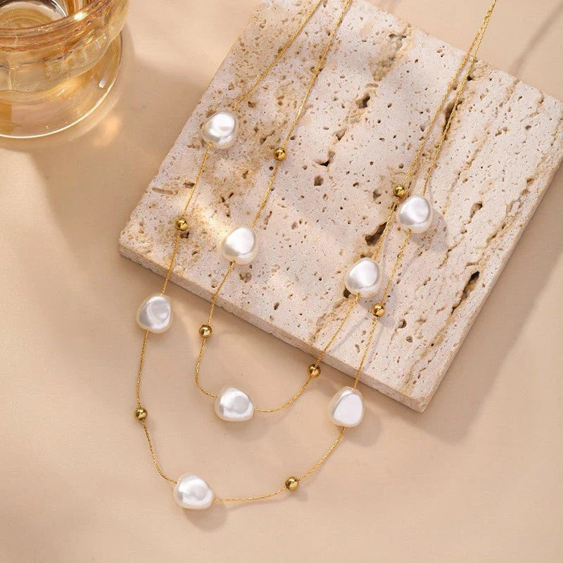 Layered pearl necklace on a stone block beside a glass
